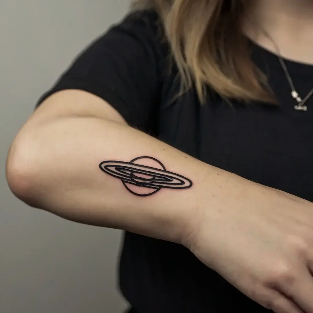 Minimalist Saturn tattoo on inner arm, featuring bold black outlines and intricate ring details, symbolizing exploration.