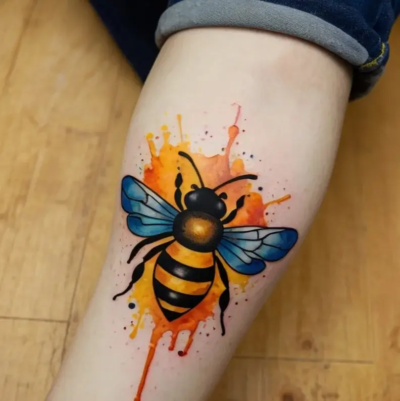 Vibrant bee tattoo with blue wings, set against a dynamic orange watercolor splash background on the forearm.