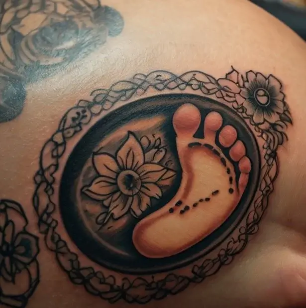 Tattoo of a baby footprint beside a flower set in an oval frame, surrounded by floral lace details.