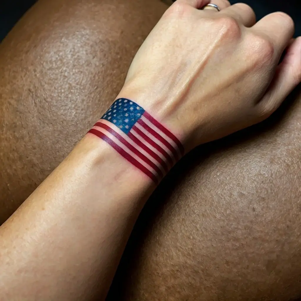 Tattoo of a realistic American flag wrapped around the wrist, showcasing the stars and stripes in vivid red, white, and blue.