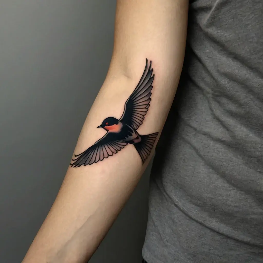 Tattoo of a flying swallow with detailed black and red shading on the forearm, symbolizing freedom and hope.