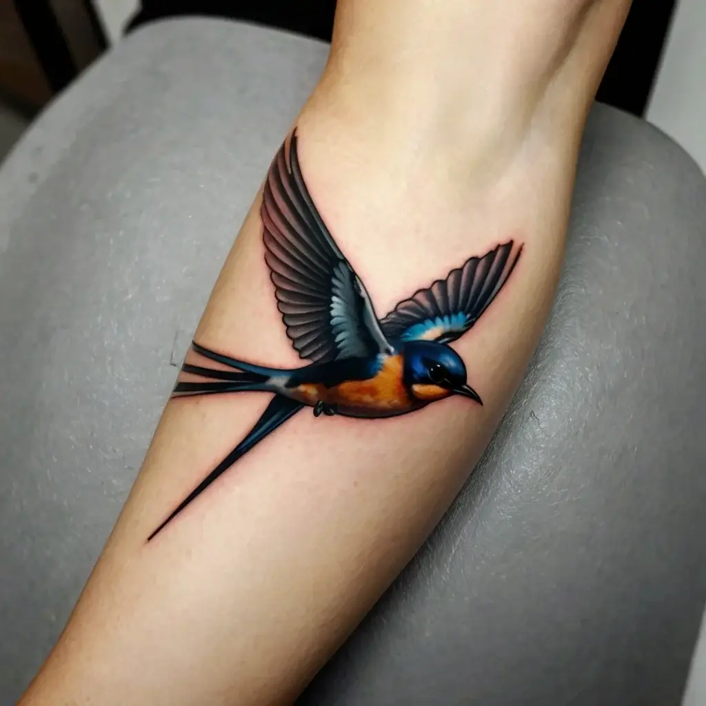 Realistic swallow tattoo with outstretched wings, featuring vibrant blue, orange, and black hues on the forearm.