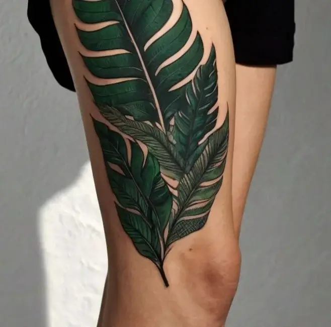 Tattoo of detailed green tropical leaves, overlapping and textured, elegantly designed on the calf.